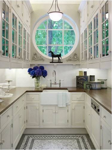 A clean kitchen with white cabinets and both circular and square windows.