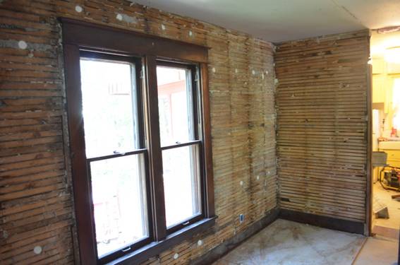 A striped wall in the interior of a house showing the slat boards around a large window.