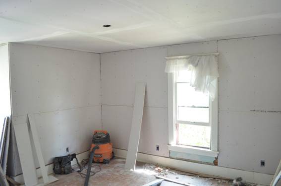 A room under construction with a vacuum cleaner and white boards leaning on the wall.