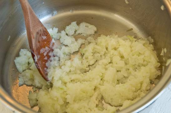A white vegetable has been mashed or diced and placed in a silver metal container with a wooden spoon.