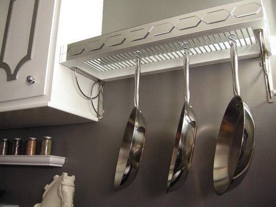 Silver pans are hanging on a white hanger on a wall.