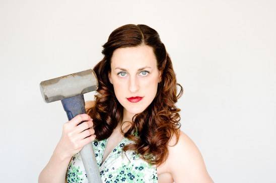 A woman holds a sledge hammer.