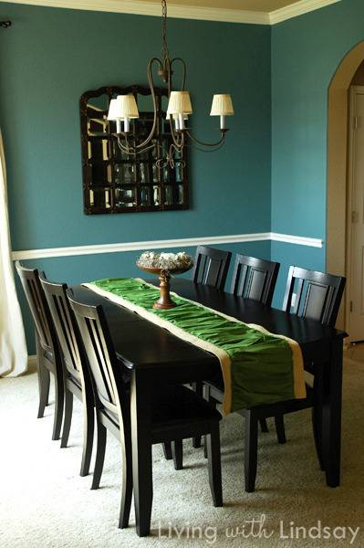 A dining room table sits next to a black picture on the wall.