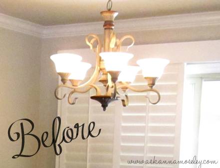 A five arm golden chandelier with white uplights hanging in front of closed white blinds.