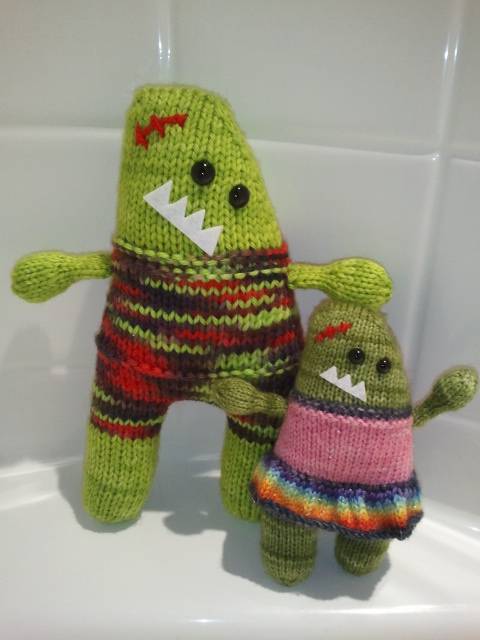 Two green handmade dolls in colorful costumes leaning on a bathroom sink.
