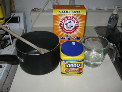 A pot on the stovetop holding a wooden spoon, with a measuring cup, baking soda and cornstarch next to it.