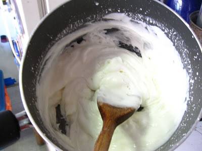 A wooden spoon is stirring white mixture in a pot.