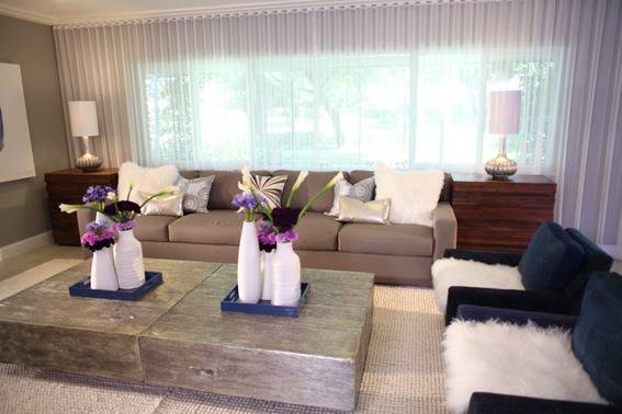 A living room with white vases on the coffee table a brown couch with throw pillows and two blue chairs with white fluffy seats