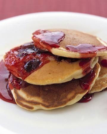 Pancakes with a berry compote drizzled on top of the plate.