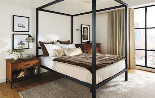 A black frame is holding a bed in a room with a full length window.
