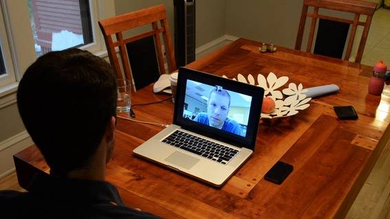 Person seeing laptop placed in a wooden dining table.