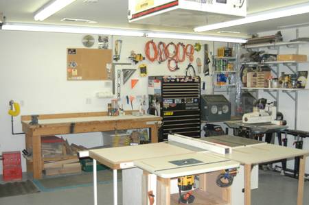 A workroom with several worktables, shelves with tools and a row of five orange extension cords on the wall.