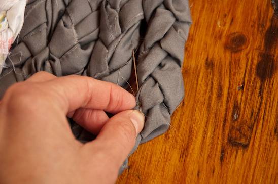 Person sewing gray color rag rug with needle and tread.