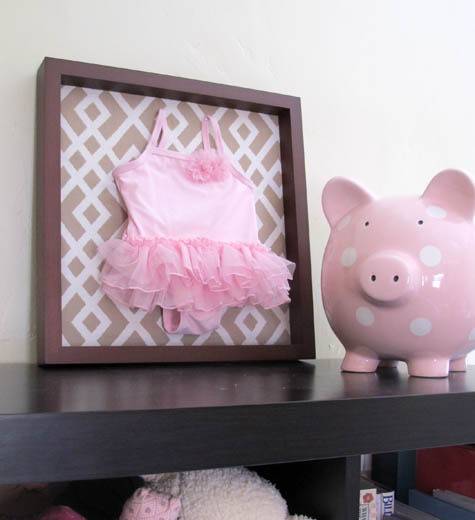 A small pink dress inside of a picture frame next to the pink Piggy Bank.