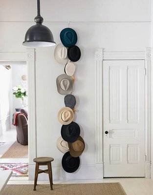 Many hats are arranged in a vertical line from floor to ceiling on a wall.