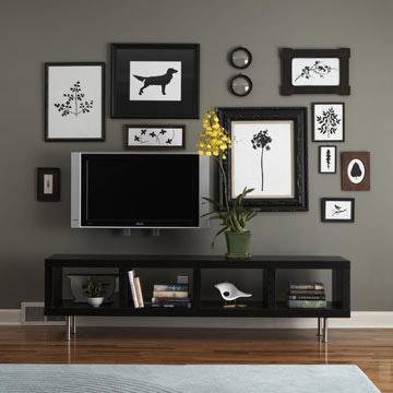 A black television table with pictures and a television hanging on a grey wall.