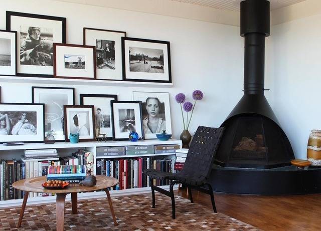 Wall full of photos next to a large, black wood stove in a living room.