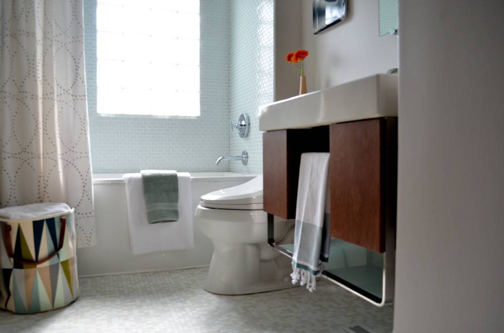 A bathroom contains a shower tub with many very small light blue tiles and a window.