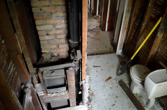 A bathroom has been partially demolished and still has a toilet, flooring, and some walls.