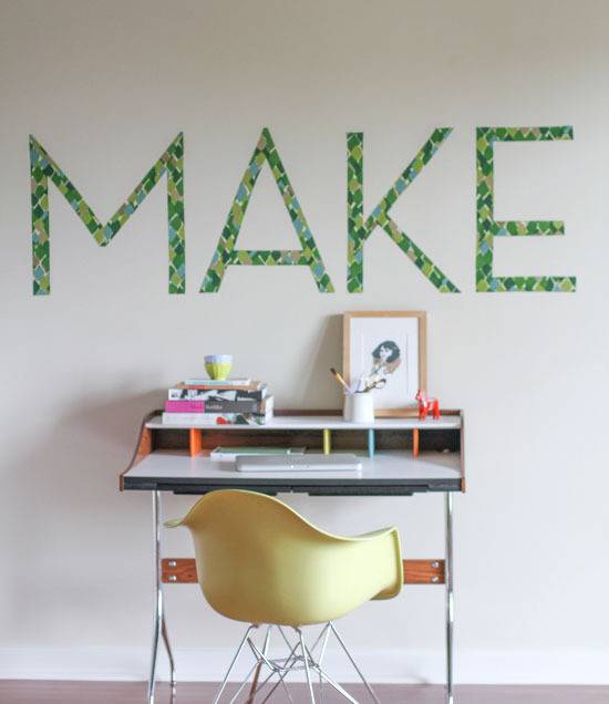 A white desk with a yellow chair in front of it with small objects on it in front of a sign that says "Make."