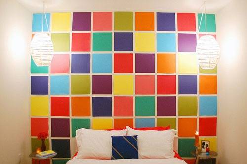 A white bed is sitting in front of a colorful wall.