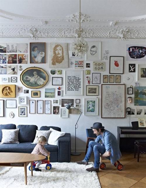 A wall in a living room is completely covered with many pieces of wall art.