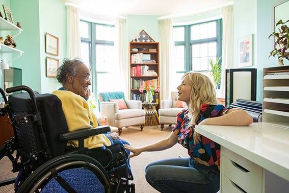 A young woman talks to an old woman who is in a wheelchair.