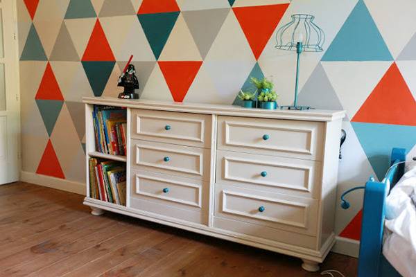 A dresser/bookcase up against a colorful triangle wall.