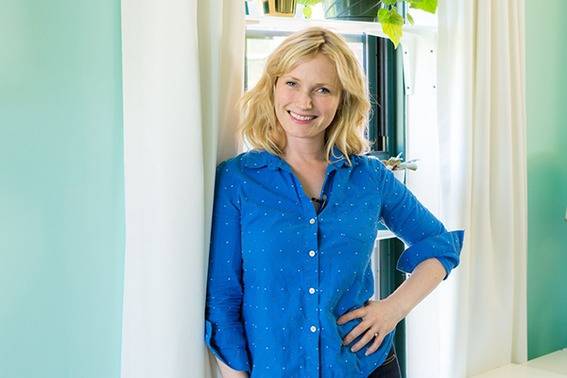 Woman in a blue blouse leaning up again the window adorned by white curtains and the walls painted teal.