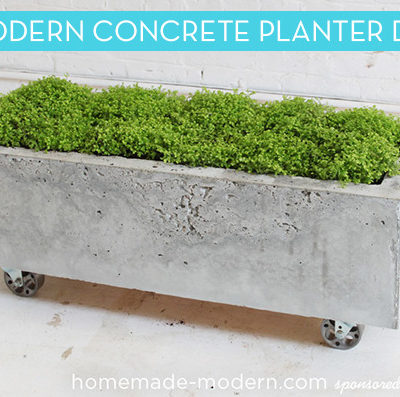 A rectangular concrete planter on wheels has a spigot pointing outward from the planter on one end.