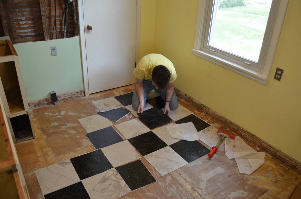 A man is on his knees putting down black and white tiles.