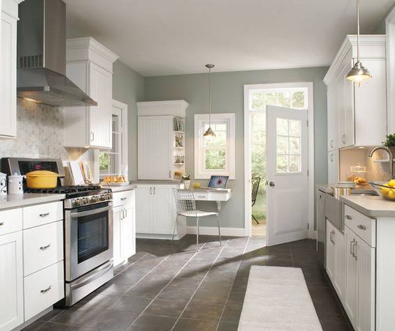 A white door opens into a kitchen with white counters and cabinets and grey walls.
