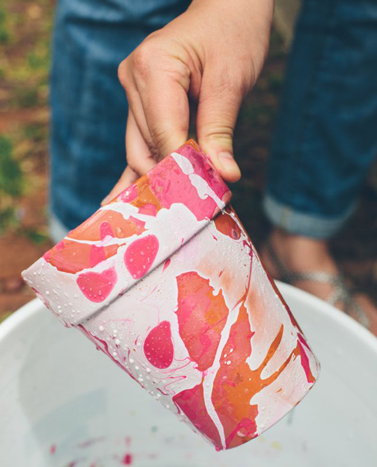 Someone is holding a flower pot that has been painted white with a pink and orange abstract design.