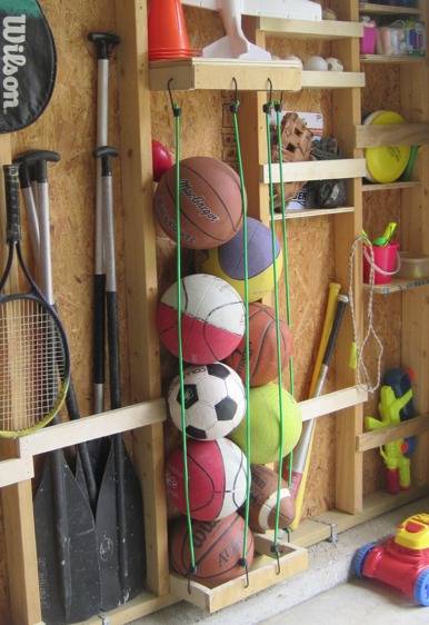 Sports balls are organized in a garage with vertical bungee cords.