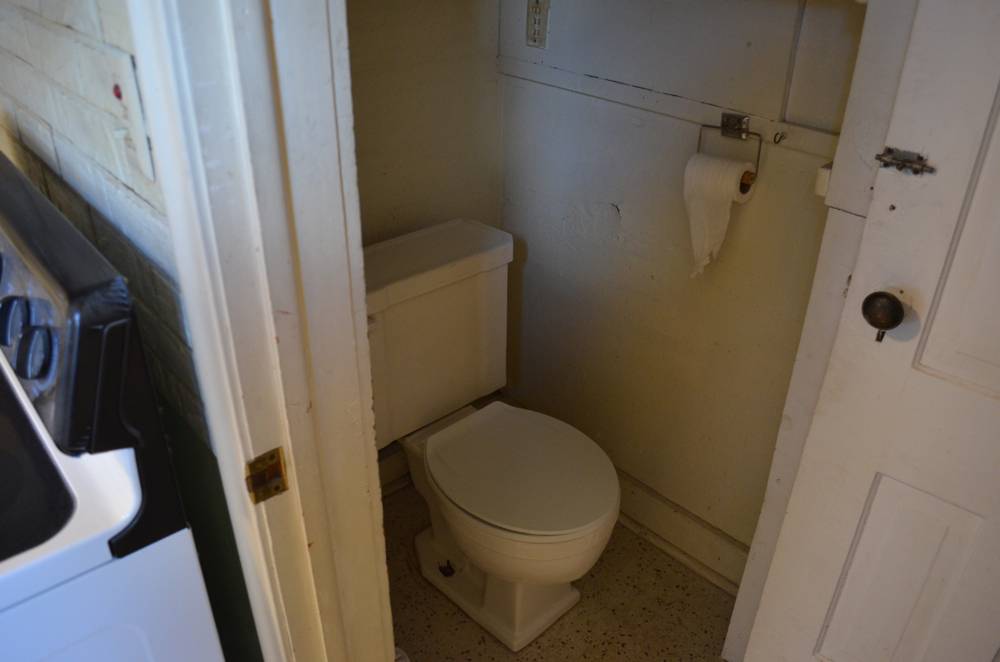 A white toilet in a tiny room with toilet paper hanging next to it.
