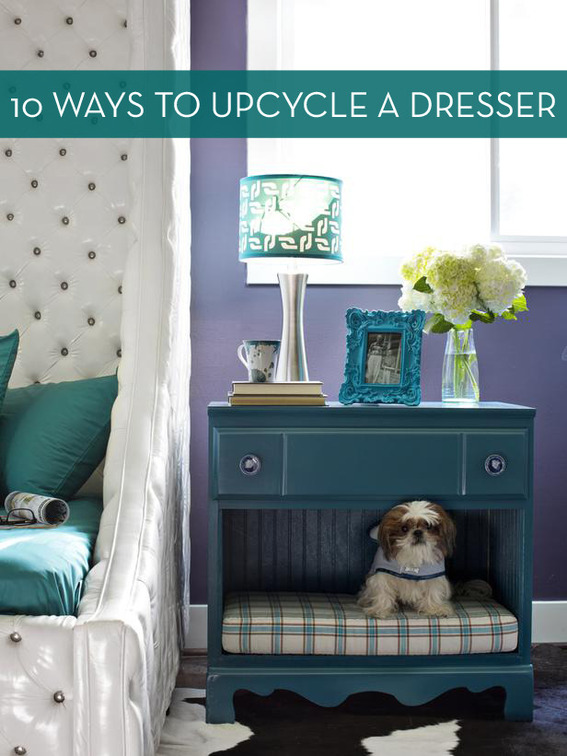 An old dresser has had some drawers removed and a small dog bed added for a fun dog hideout that doubles as a nightstand with a lamp, vase, and framed photo on top.