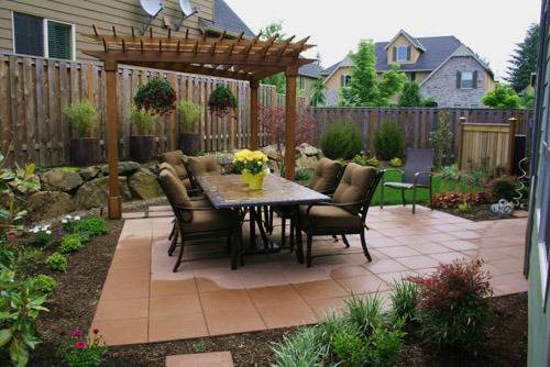 An outdoor dining table sits on a tile patio with a pergola nearby.