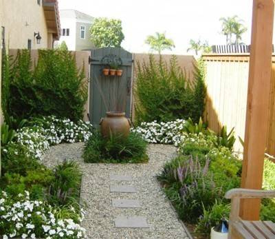 A backyard contains a circular path and planned landscaping with gravel rocks and low growing shrubs and vines.