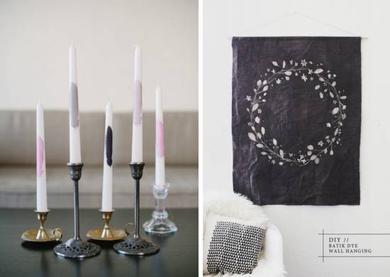A collection of taper candles in brass, pewter looking and glass holders and a gray wall hanging picturing a white wreath.