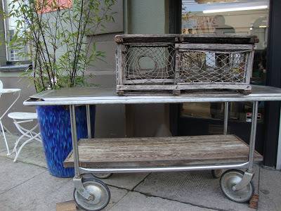 A cart with a silver top has a couple of wire mesh and wooden crates on top of it.