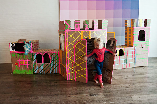 A child in a Spiderman costume rushes out of the cardboard castle.