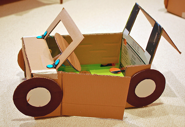 A cardboard car with brown tires, a green floorboard and an open door.