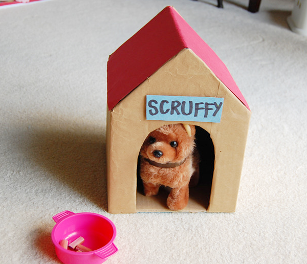 A pink bowl outside a small brown doghouse with a red roof, the word scruffy on a blue sign on the front and a toy dog in it.