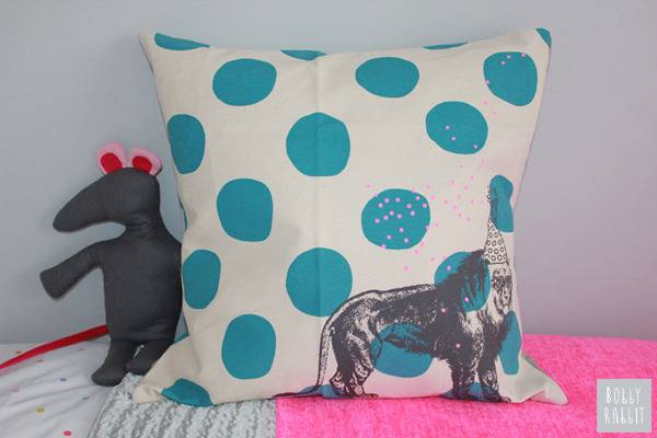 A child's bedroom has a square pillow that is white with blue dots and an animal.