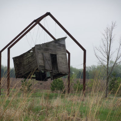 A small building is levitating between the field and a frame.