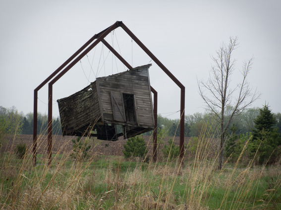 A small building is levitating between the field and a frame.