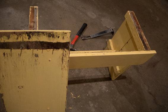 An old yellow piece of furniture is partly disassembled and sits next to hand tools.