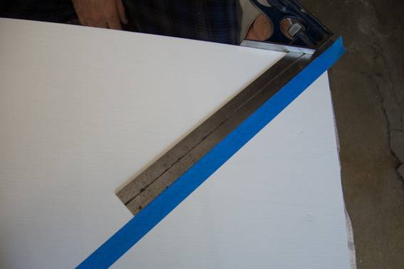 A ruler demarcates a diagonal line on a white piece of wood, and painter's tape has been applied to the wood next to the ruler.