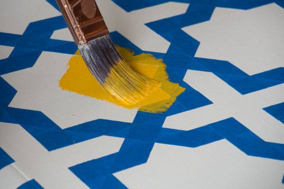 A white and blue tile pattern with yellow paint being put on it.