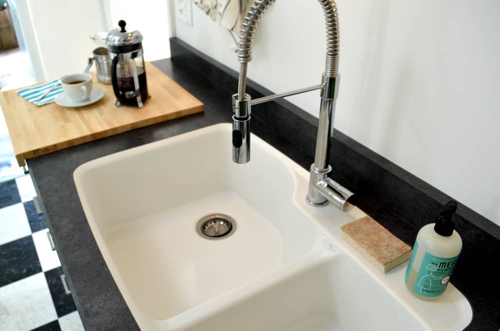 A white basin is set in a black counter in a kitchen with a black and white checkered floor.